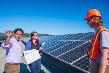 three people standing in front of a solar array