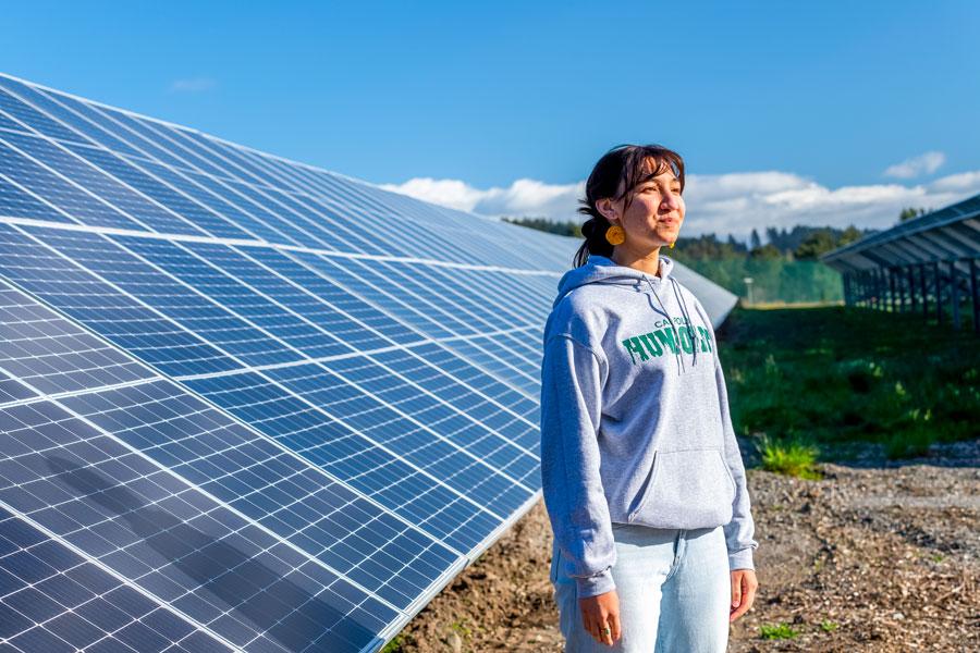 a student looking in the distance standing in front of a solar array